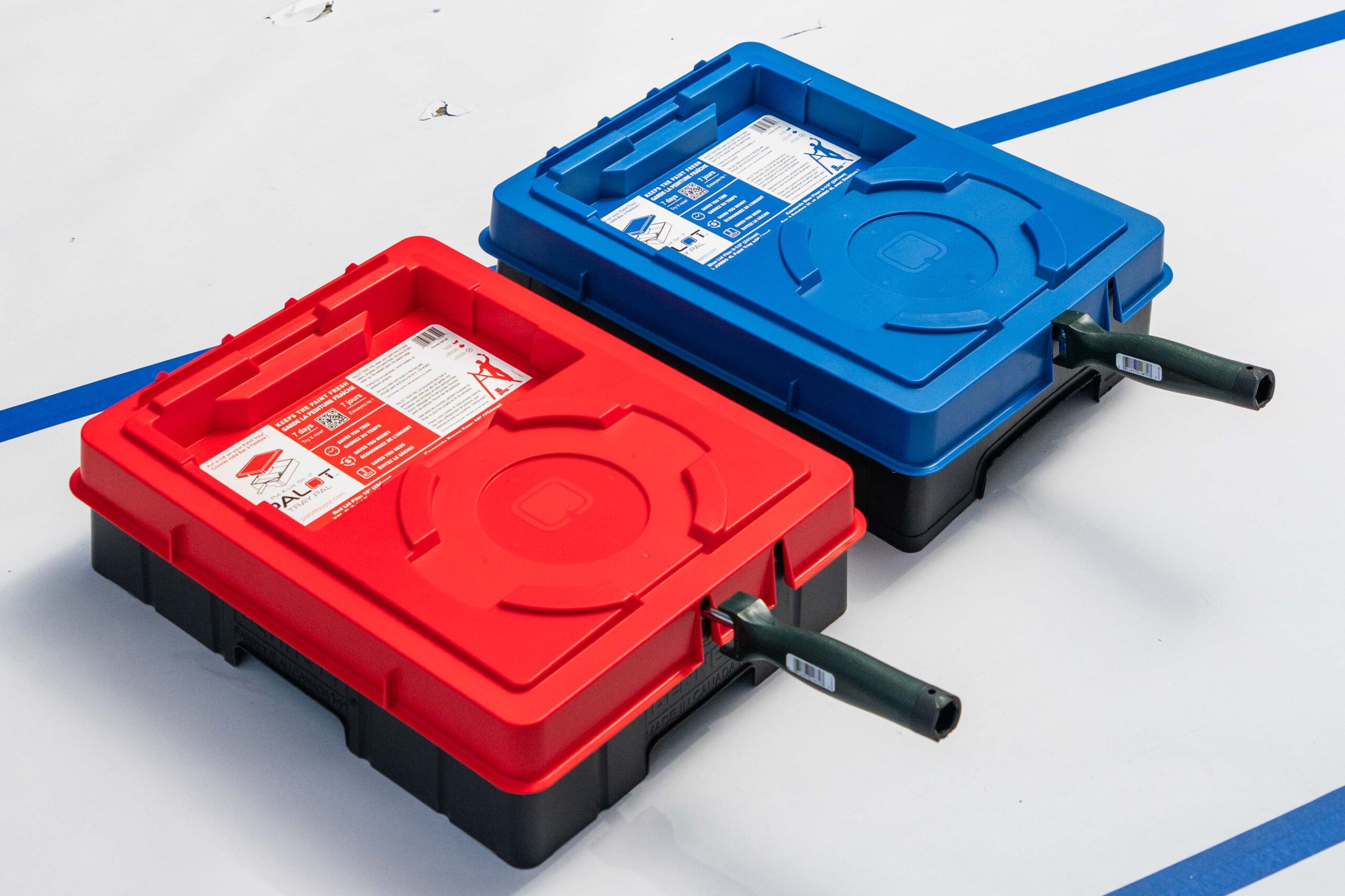 Red & Blue PALOT TRAY PAL lids closed 2 paint trays sit on the floor of a room being painted. On top of each is a Blue or a Red PALOT TRAY PAL LID keeping the paint roller sealed in.